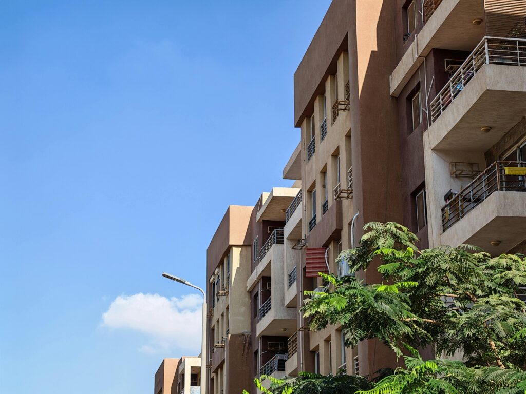 pexels-photo-34789470-34789470 Urban apartment building against a bright blue sky with foliage in the foreground.
