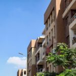 Urban apartment building against a bright blue sky with foliage in the foreground.