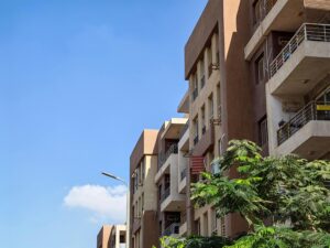 Urban apartment building against a bright blue sky with foliage in the foreground.